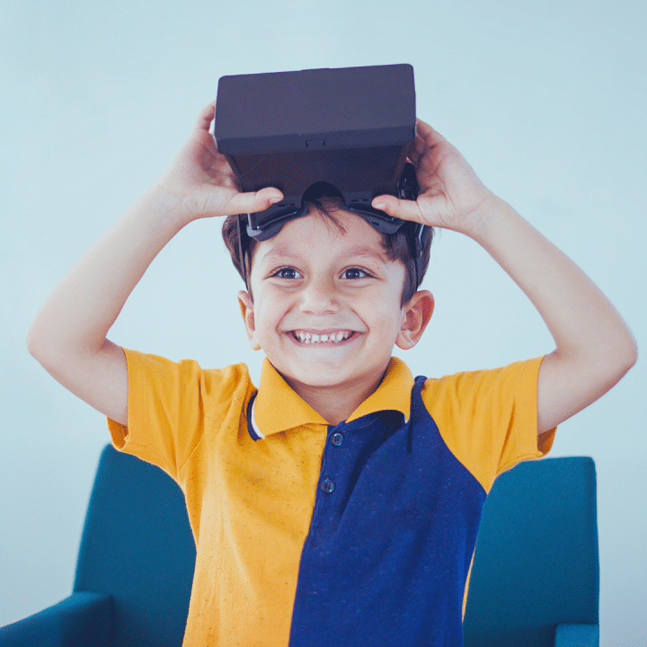 Kuvassa pieni tummatukkainen poika hymyilee iloisesti virtuaalilasit otsalla